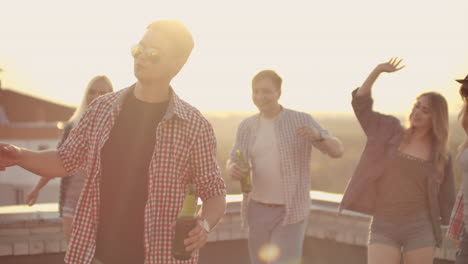 A-young-boy-in-trendy-glasses-with-beer-moves-in-a-dance-at-a-party-with-his-friends-on-the-roof.